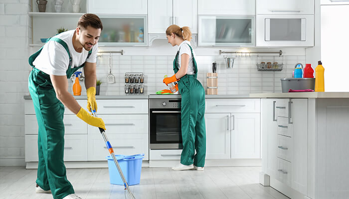 Cleaning and Sanitation Equipment - Food Fun Trip - FoodFunTrip Two cleaners in green overalls mop a bright white kitchen; a blue bucket sits nearby as one person wipes the floor while the other works at the counter near the oven.