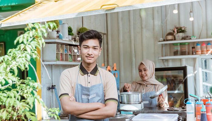 Young entrepreneurs operating a small food business from a home-based kitchen, preparing meals and serving customers while managing daily food business operations.