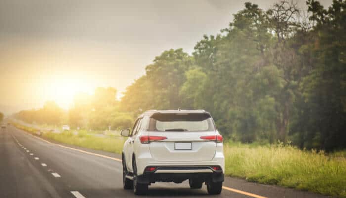 How to Drive Defensively on Kentucky Highways- Food Fun Trip - FoodFunTrip White SUV driving along a rural Kentucky highway at sunset, surrounded by lush green roadside vegetation and dense trees, representing scenic Kentucky backroad travel conditions often seen on state highways and long-distance rural routes.
