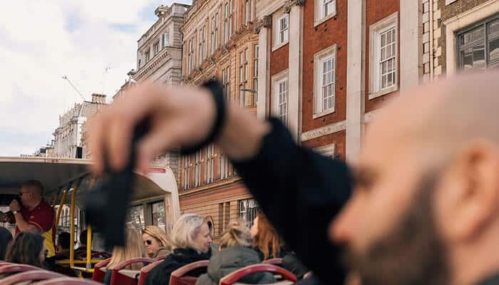 A Different Side Of Londons History - Food Fun Trip - FoodFunTrip Passengers on an open-top sightseeing bus along a city street with brick-era buildings.