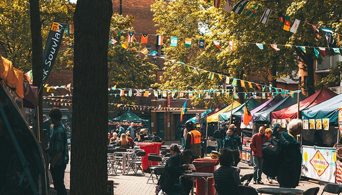 Good Communication Solves Problems Before They Become Bigger Ones - Food Fun Trip - FoodFunTrip Outdoor festival street market with colorful bunting, stalls, and people sitting at tables in the sun.