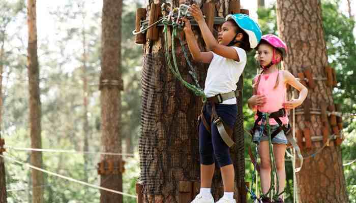 Nearby Travel Ideas - Food Fun Trip - FoodFunTrip Children wearing helmets and safety harnesses navigating a tree-based ropes course, illustrating outdoor adventure activities that travelers may combine with a Nova Adventure Park visit.