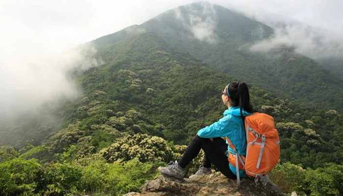 Match Your Clothing and Footwear to Conditions - Food Fun Trip - FoodFunTrip Backpacking Tips CWBiancaVoyage From ConversationsWithBianca showing a female hiker with an orange backpack resting on a rocky viewpoint overlooking misty green mountains.