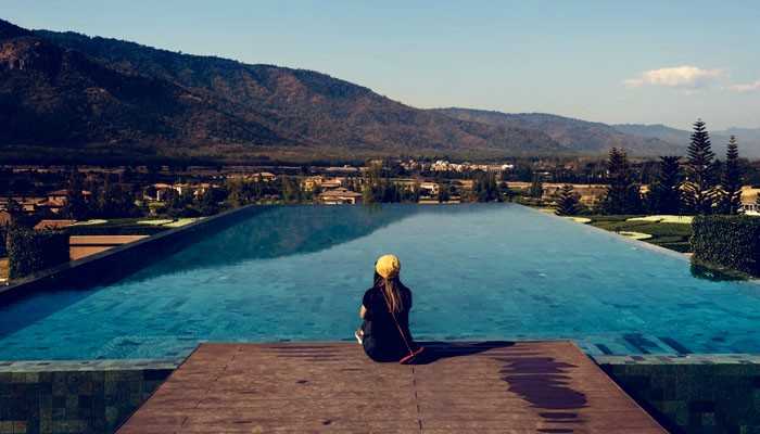 Things to Do Near Alvord Hot Springs - Food Fun Trip - FoodFunTrip Woman sitting beside a scenic infinity pool overlooking mountains and lush landscapes, highlighting relaxing resort experiences and outdoor attractions near Alvord Hot Springs in Oregon.